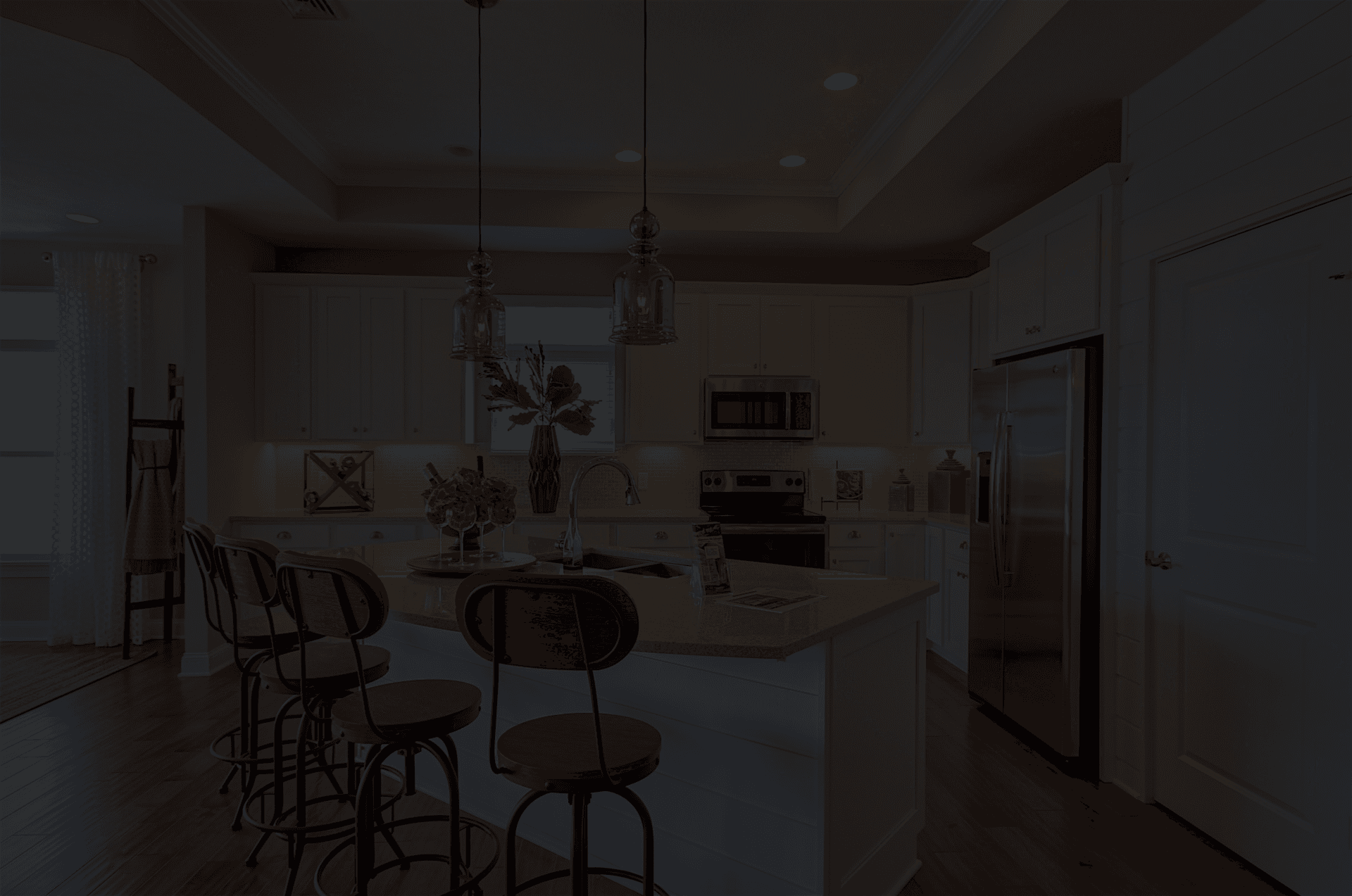Modern kitchen with wooden floors, white cabinets, and a central island. Three bar stools, pendant lights, and stainless steel appliances add elegance.