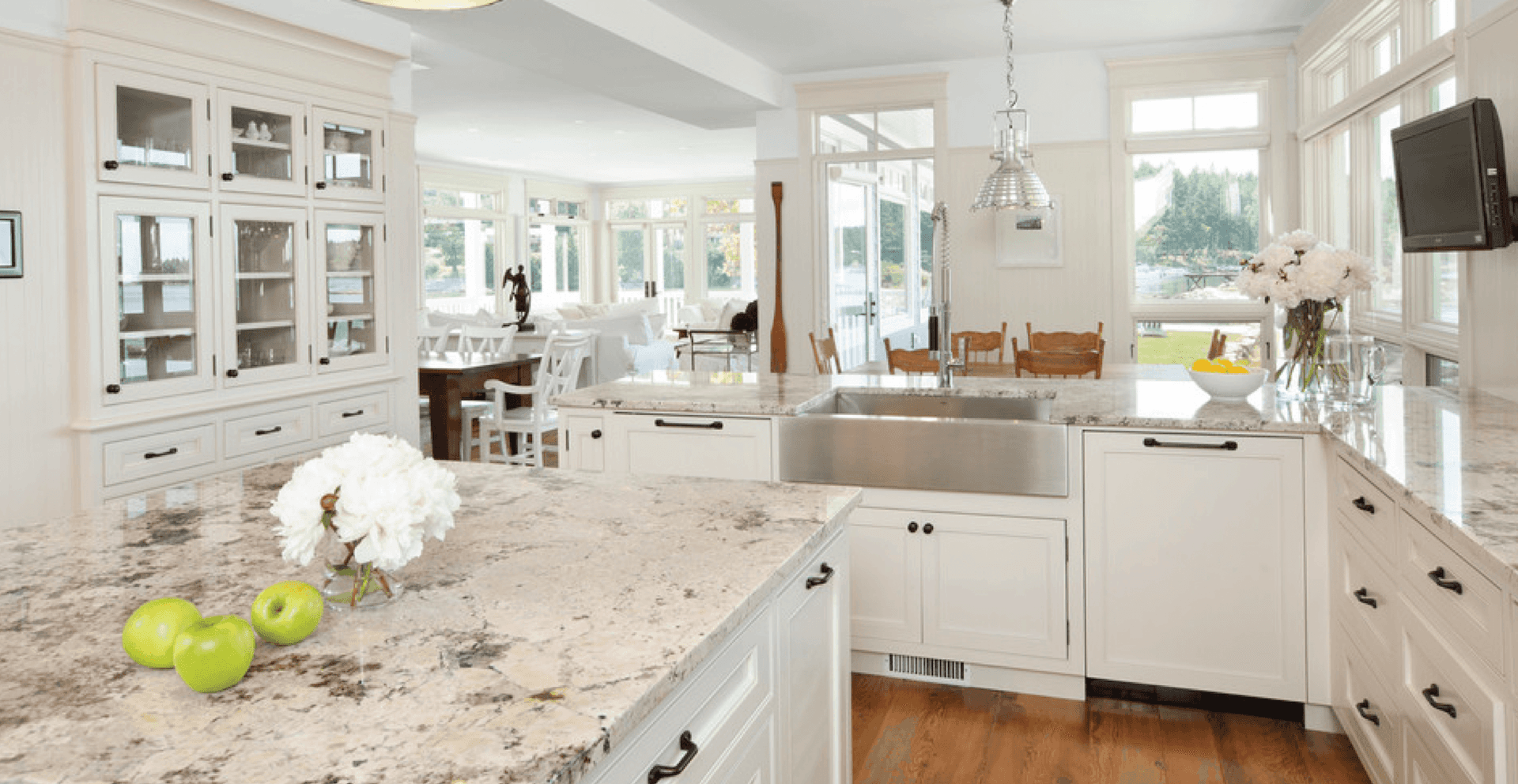 Spacious kitchen with white cabinets, granite countertops, and stainless steel sink. Green apples and flowers add fresh accents. Bright and inviting.