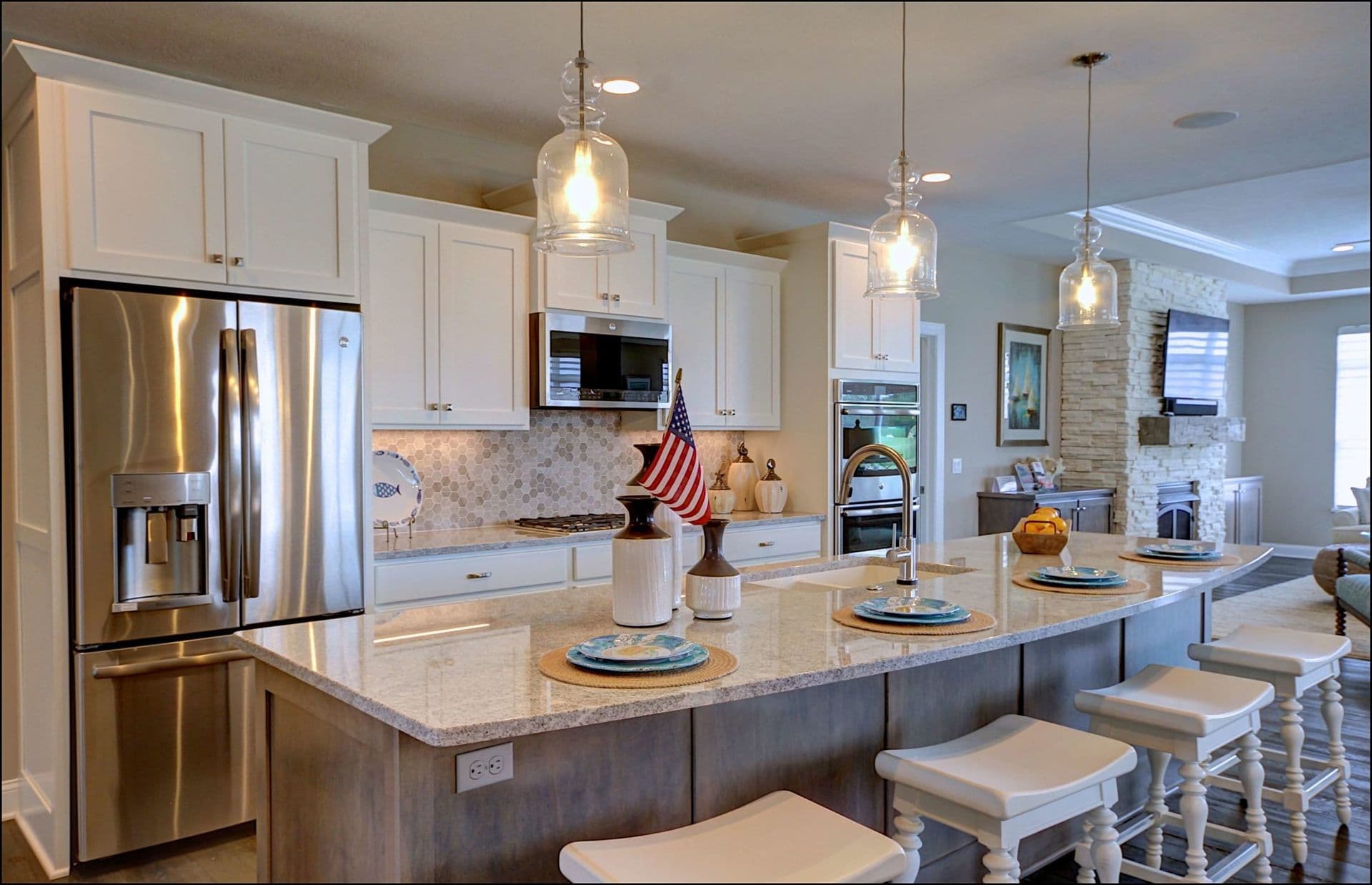Modern kitchen with white cabinets, stainless steel appliances, and a marble island with stools. Pendant lights hang above, creating a welcoming ambiance.