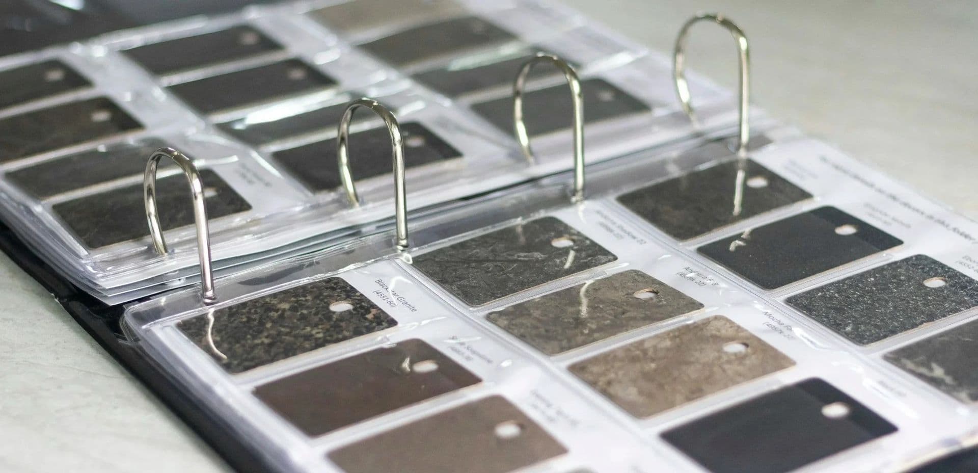 Open binder with stone samples in plastic sleeves. Each sample varies in texture and shade, from dark gray to black. The tone is organized and professional.
