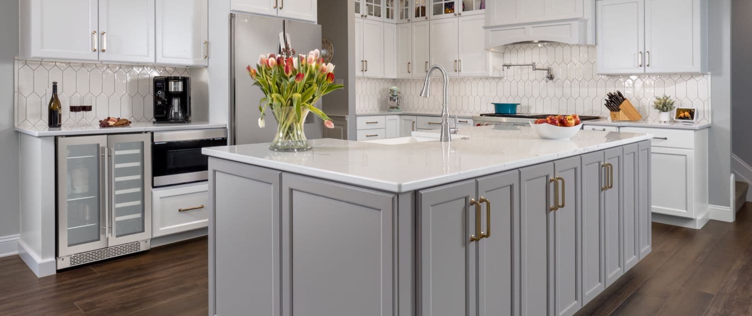 Modern kitchen with white cabinets, a large gray island with a vase of tulips, stainless steel appliances, and hexagonal backsplash. Bright and inviting.